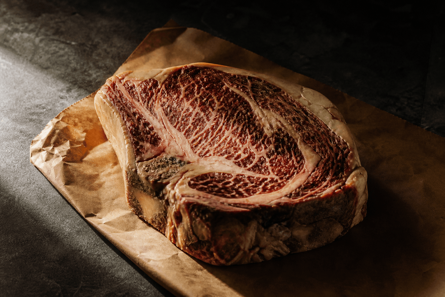 Dry-aged ribeye on unprinted butcher paper, deep marbling in soft window light